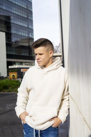 Portrait of serious young male in bright hoodie leaning on wall outside