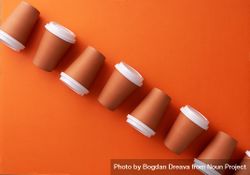 Diagonal row of disposable coffee cups on orange background 56kWl4