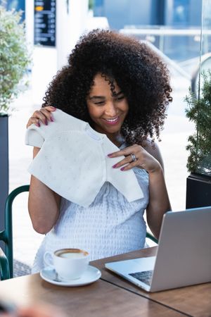Smiling pregnant Black woman showing baby booties to laptop
