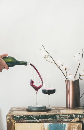 Wine glasses being poured from bottle with dried cotton in vase, vertical composition, copy space