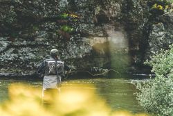 Confident man fishing with rod while standing in river stream