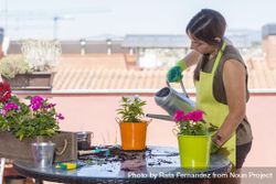 Young woman wearing a gardening apron watering a plant on balcony bGRKjx
