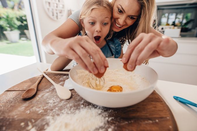 Excited young girl watching egg pour out of shell in kitchen