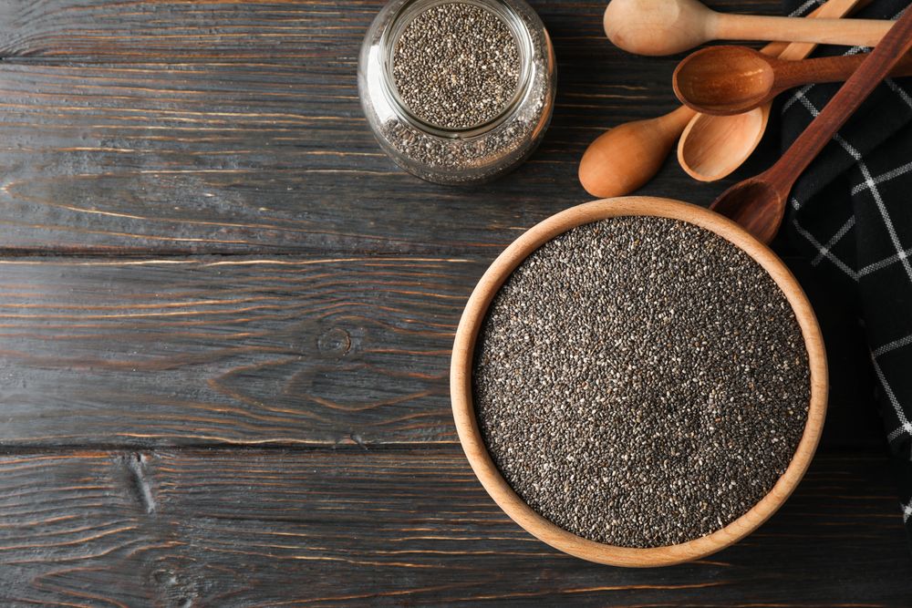 Chia in wooden bowl on wood background, top view