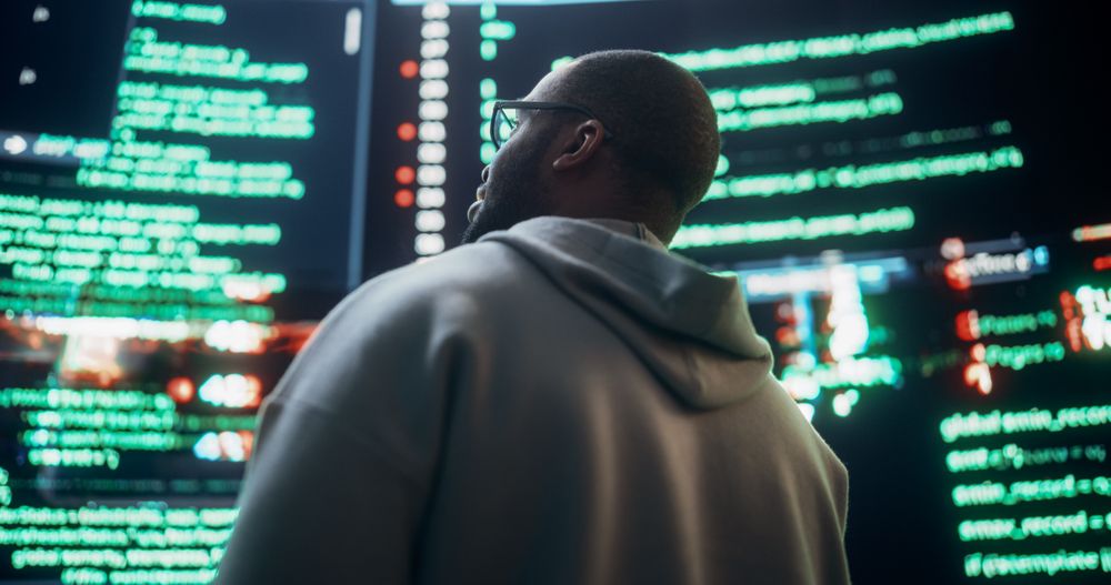 Close Up Back View of Young Black Man Looking at Big Digital Screens Glitching While Displaying Code Lines.