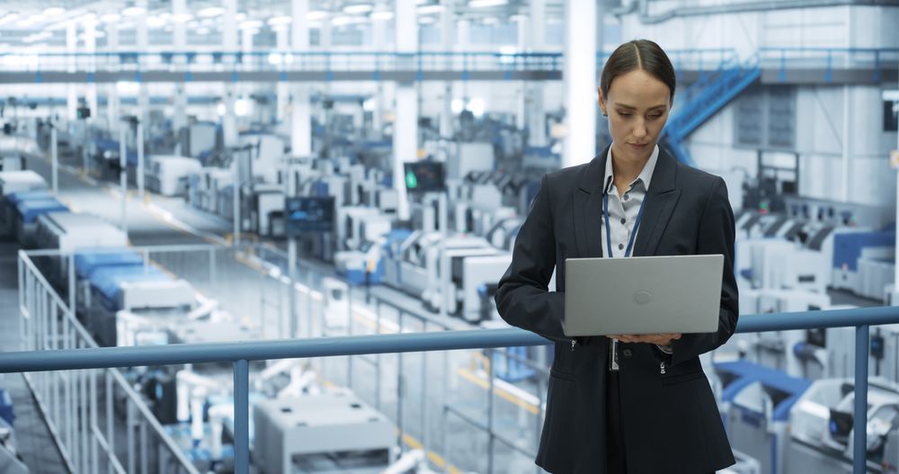 Electronics Manufacturing Technician Working on a Laptop Computer at a Factory Space. Female Specialist Developing, Maintaining, Upgrading Programs for Machine Production and Assembly