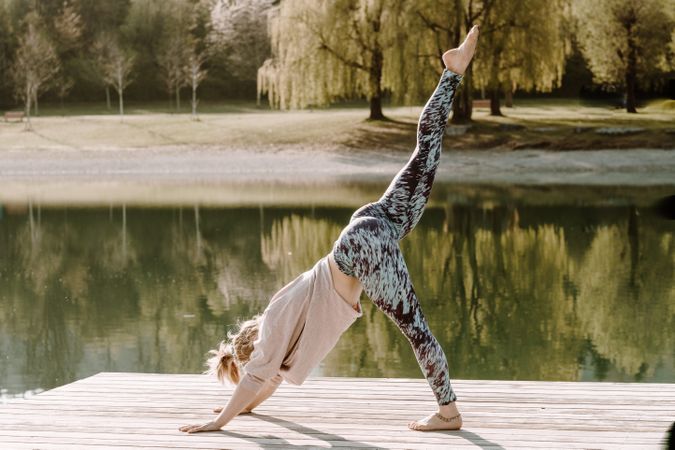 Woman doing yoga pose on wooden dock beside lake