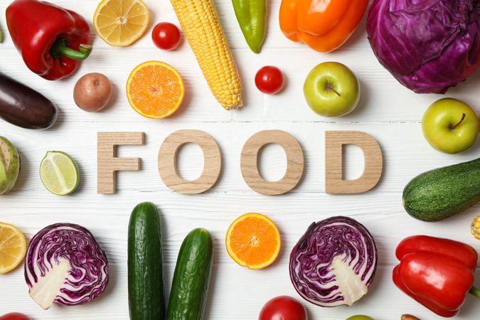 Word Food laid out of wooden letters, vegetables and fruits on wood background, top view