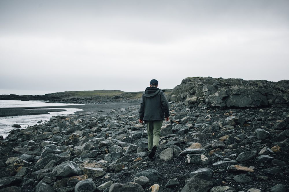 Back of man walking on rocky beach on overcast day