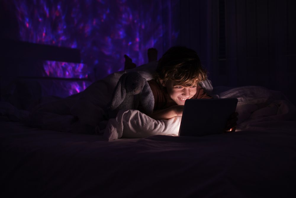 Happy boy watching video on tablet in dark bedroom