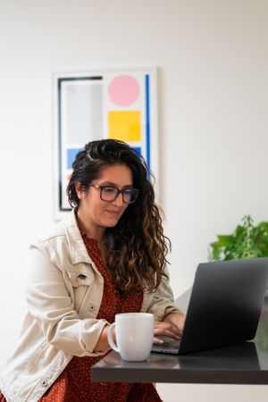 Woman working at laptop at table with coffee