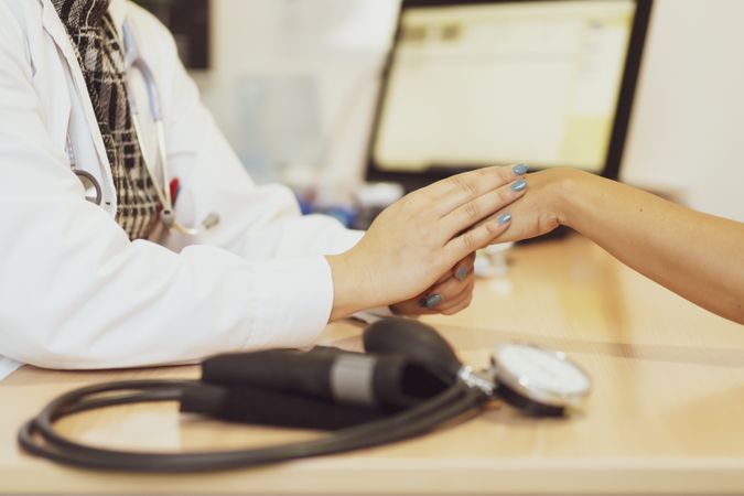 Doctor holding hand of patient at table with pulsometer