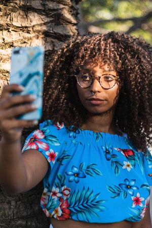 Glad Black woman taking selfie near palm
