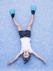 Adorable boy in snorkeling mask and flippers lying on pool