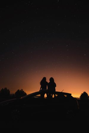 Back view silhouette of two people sitting on top of car at night