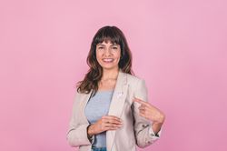 Smiling woman wearing a pink breast cancer awareness ribbon while pointing at it.