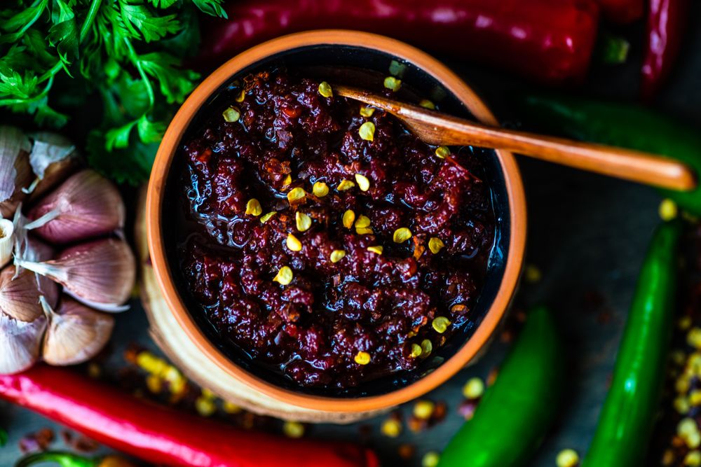 Close up of pot of traditional Georgian sauce Adjika with garlic bulb & raw ingredient