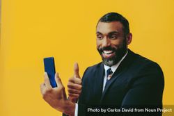 Happy Black businessman in suit speaking at smartphone screen while giving the thumbs up 5zqGj0