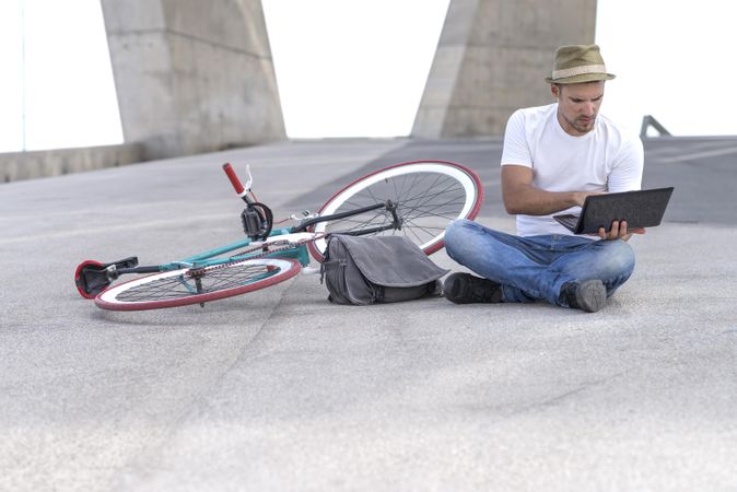 Male sitting outdoors with bicycle and using laptop