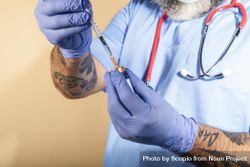 Tattooed healthcare worker with stethoscope on neck holding a syringe 5RzrO5