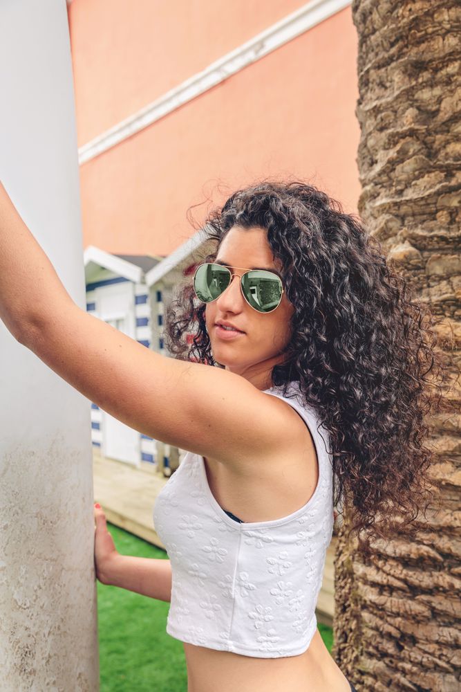 Brunette surfer woman in sunglasses and bikini holding surfboard