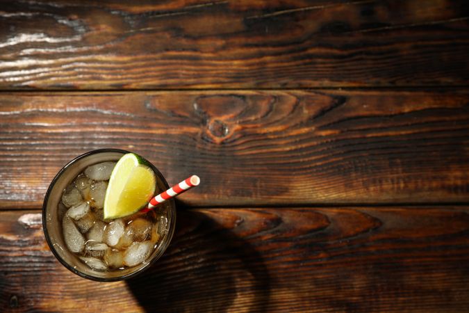 Glass with ice cola and lime slice on wooden background