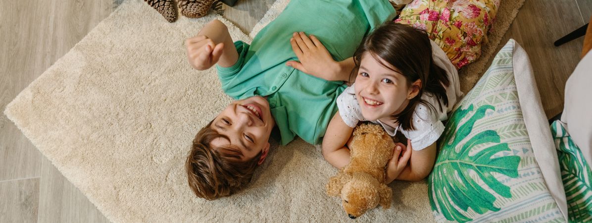 Banner of children laughing and relaxing lying over rug in a cozy ambiance at home