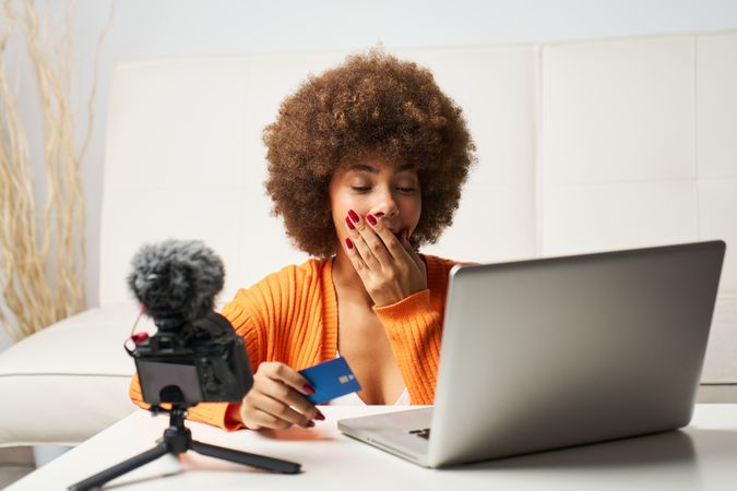 latina woman with afro hair surprised while shopping online with laptop and paying by credit card