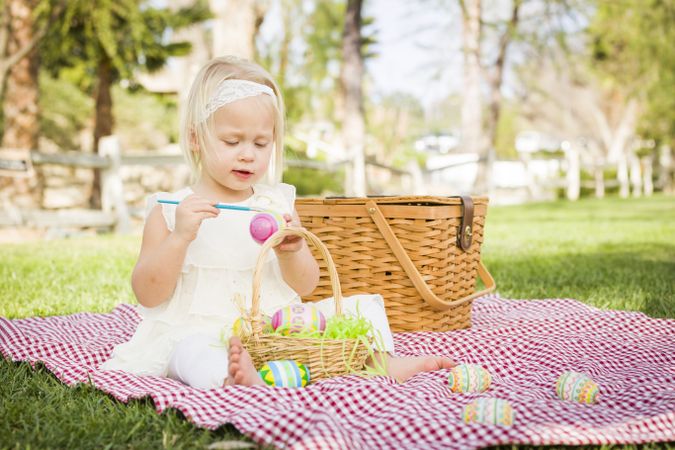 Cute Baby Girl Coloring Easter Eggs on Picnic Blanket