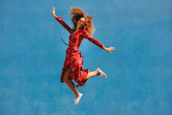 Young female model in red sundress jumping with joy