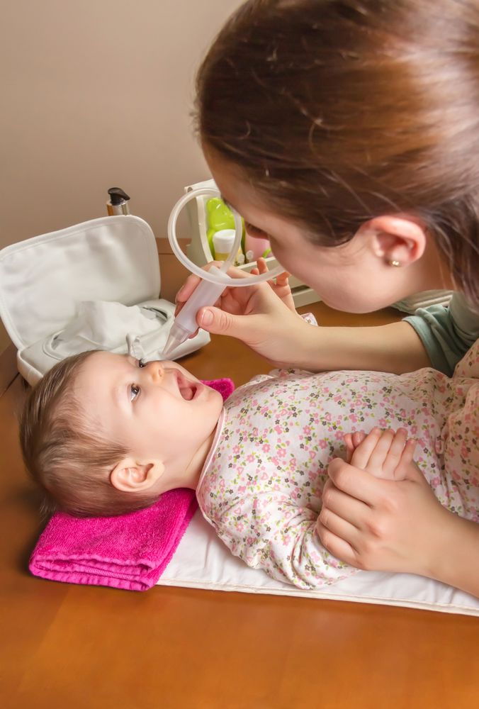 Baby entertained by nasal aspirator with mother