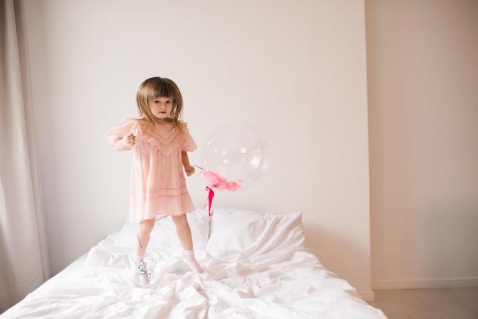 Girl in pink dress with balloon jumping on bed