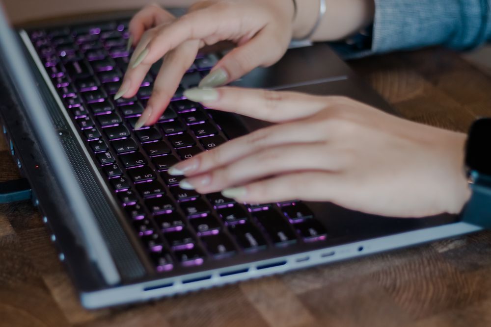 Female hands typing on a modern laptop with illuminated keyboard