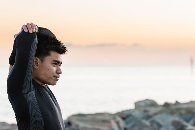 Asian sportsman stretching shoulders near sea