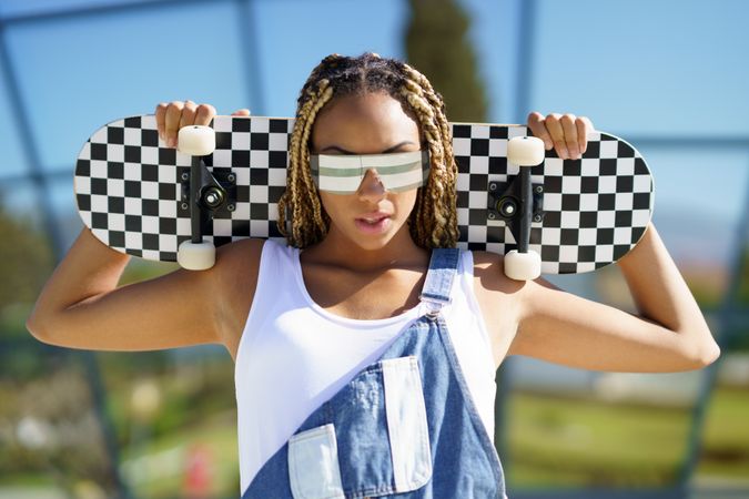 Female in denim overalls with checkered skateboard behind her head