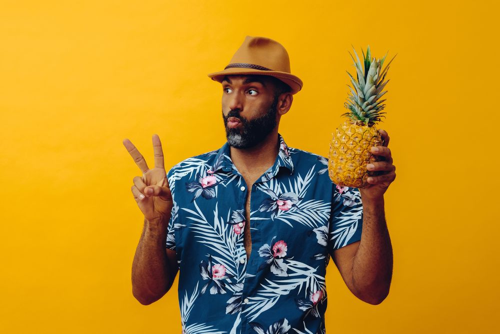 Surprised male holding a pineapple up in yellow studio