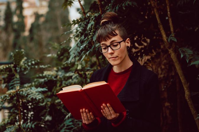 Young woman reading book on bench in park