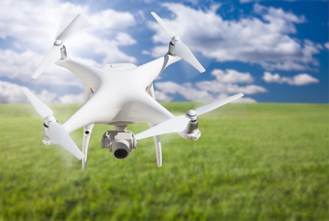 Unmanned Aircraft System (UAV) Quadcopter Drone In The Air Over Grass.