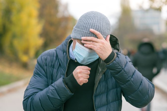 Man with facemask and knit cap putting his hand on his head