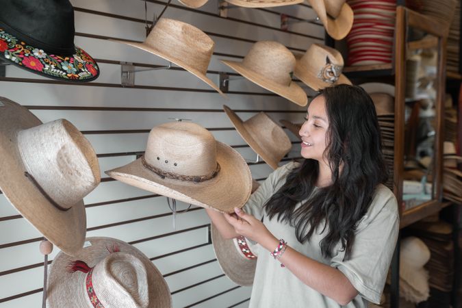 A young Hispanic woman is choosing a hat in a shop