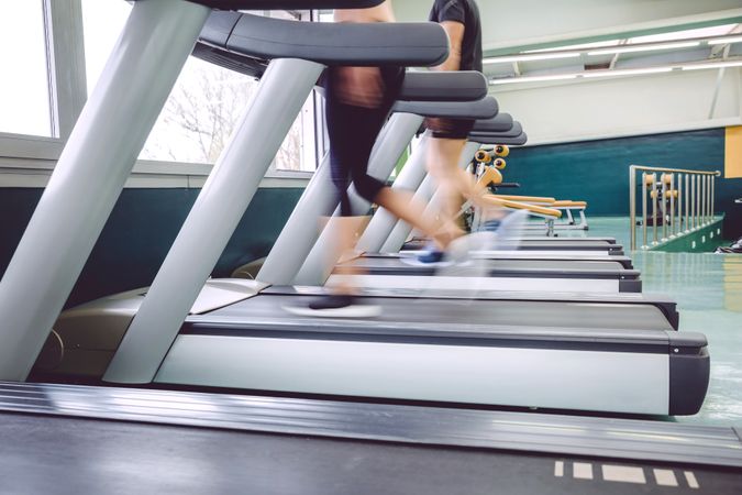 Feet of two people jogging in motion on row on treadmills in gym