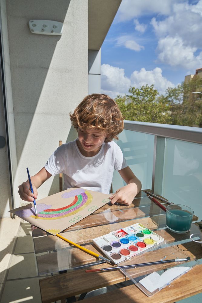 Cheerful boy drawing rainbow on terrace