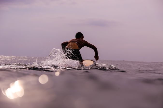 Man on surf board floating on water and cloudy sky