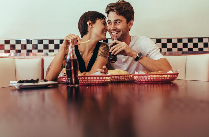 Romantic couple sitting in a diner with food and soft drinks on the table