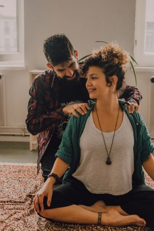 Man rubbing shoulders of joyful woman resting on floor at home