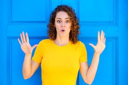 Surprised woman in yellow dress against a closed blue door