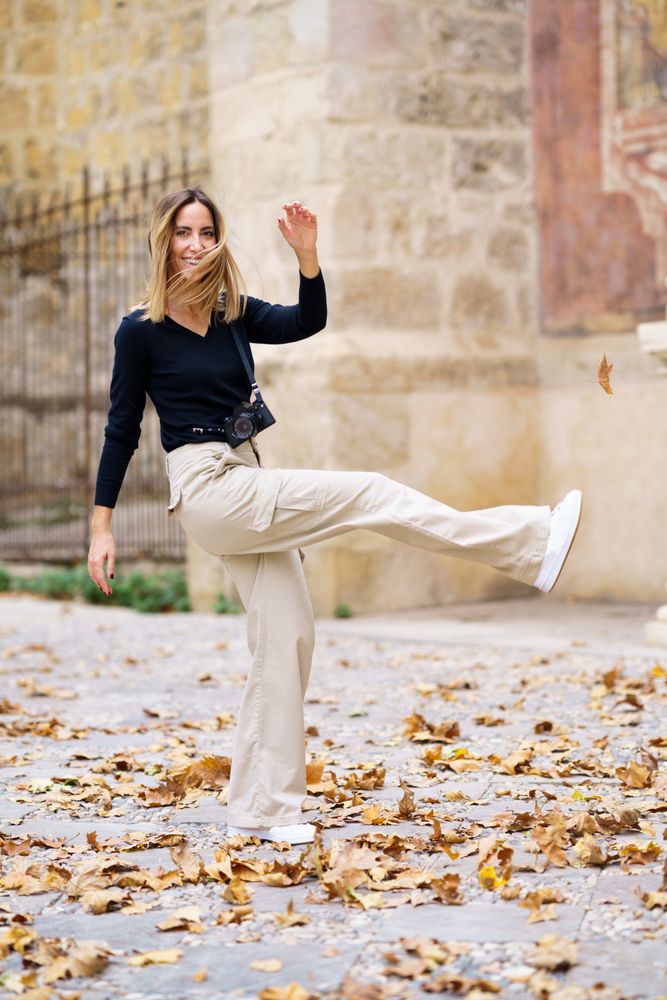 Joyful female tourist kicking fallen leaves during walk in park