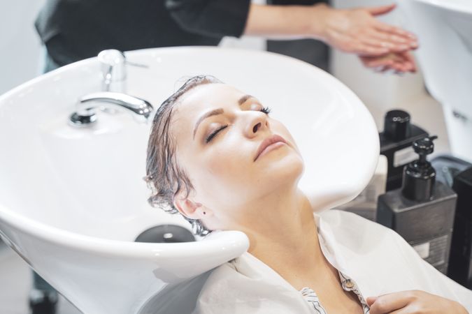 Stylist washing hair of client in basin
