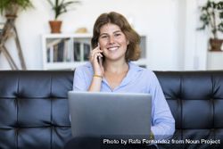 Female entrepreneur sitting on couch at home using a laptop and speaking on phone 4d8a6N