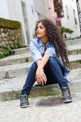 Confident female with curly hair sitting on cement stairs outside